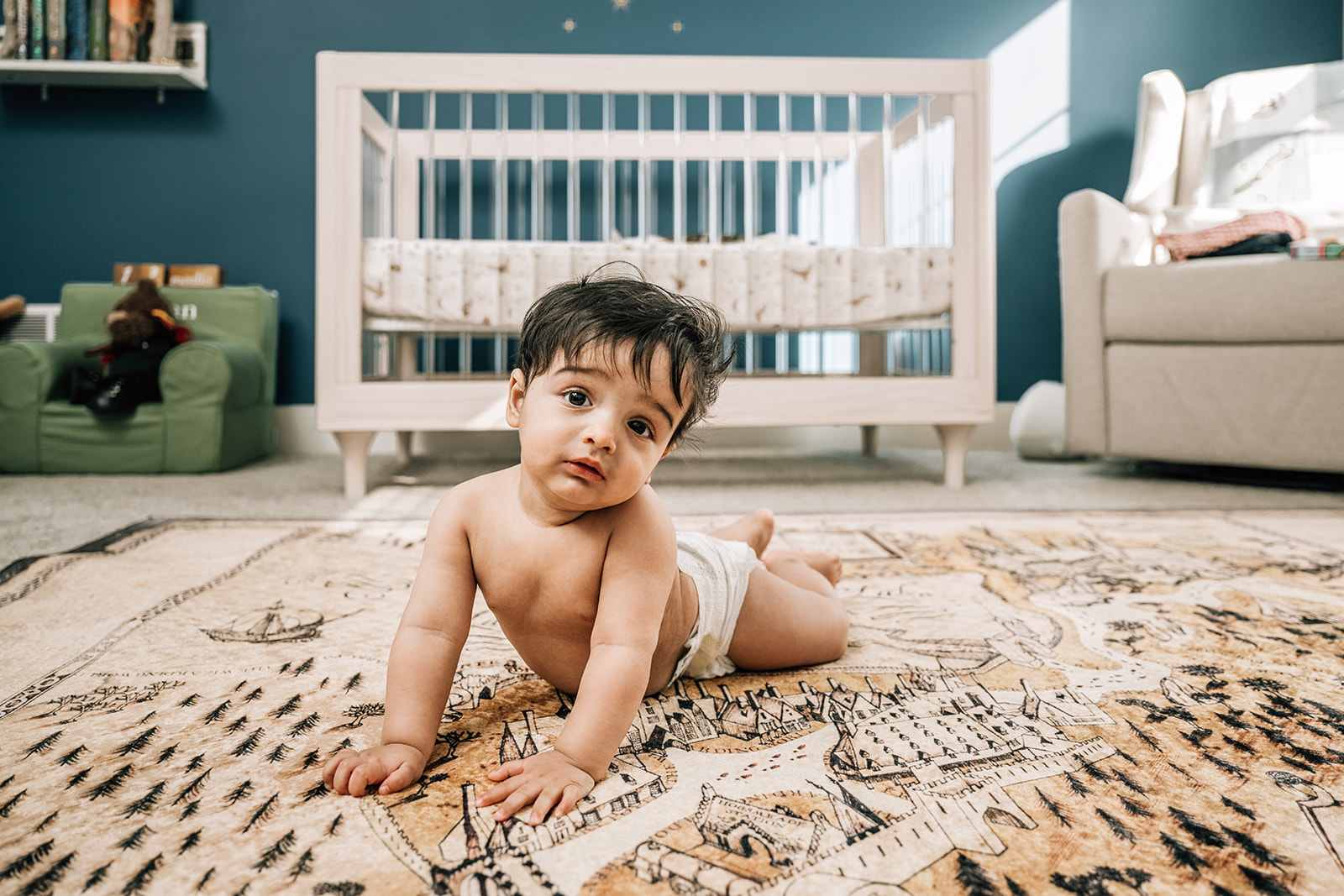 Baby sitting on nursery rug during milestone session, part of the first year of newborn photos.