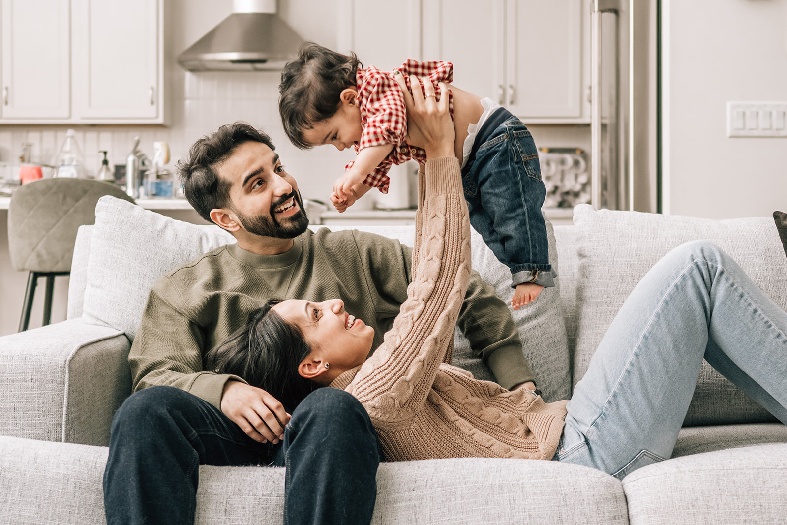 Parents playing with toddler on couch, capturing connection during the first year of newborn photos.