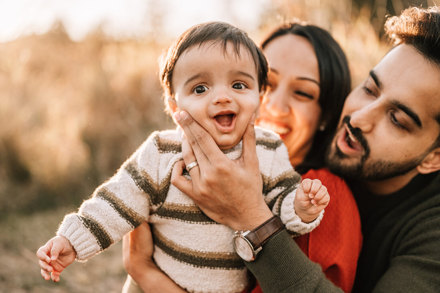 Happy baby held by parents during outdoor milestone session, part of the first year of newborn photos.