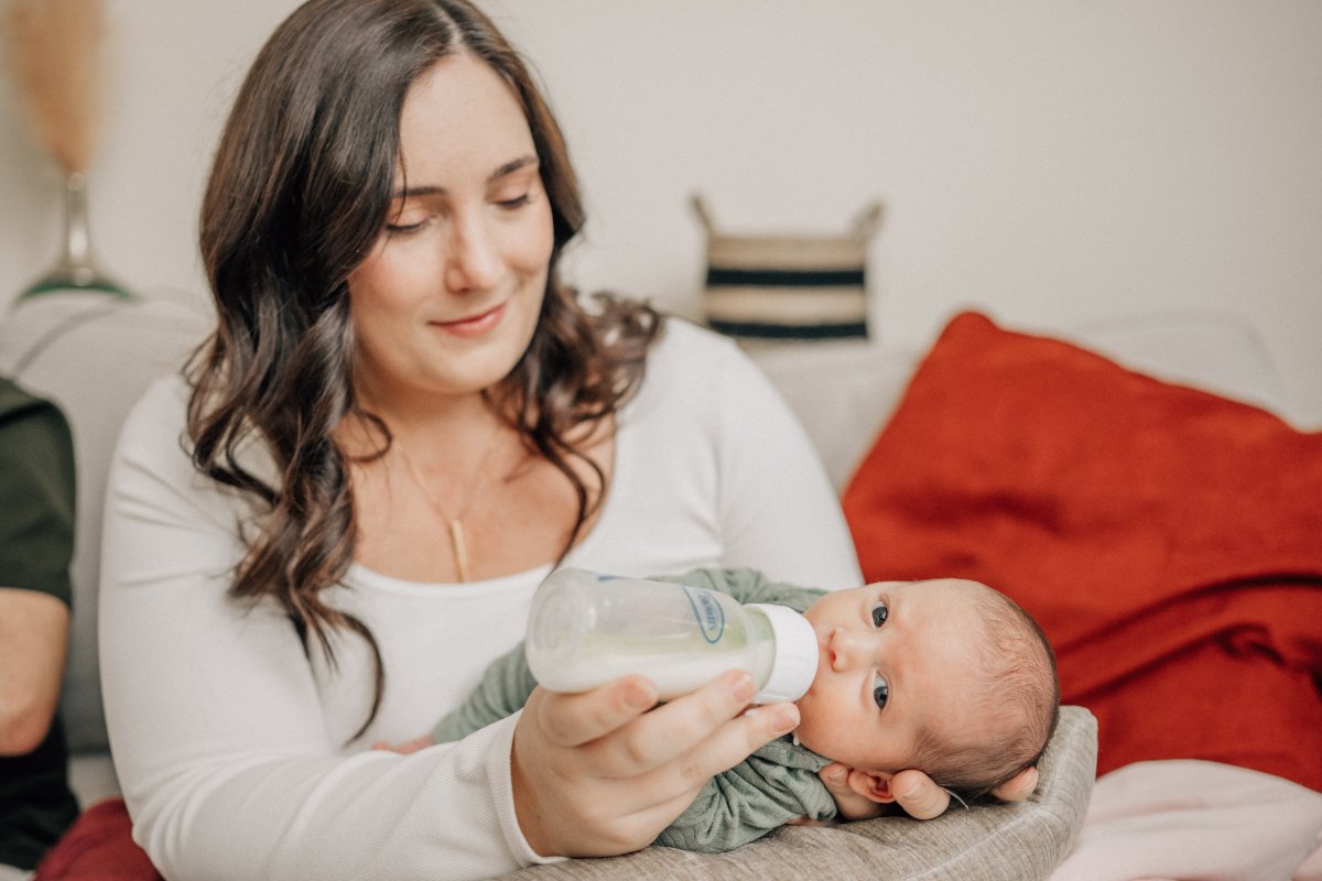 Parent bottle-feeding a newborn on the couch during an in-home newborn photography session.