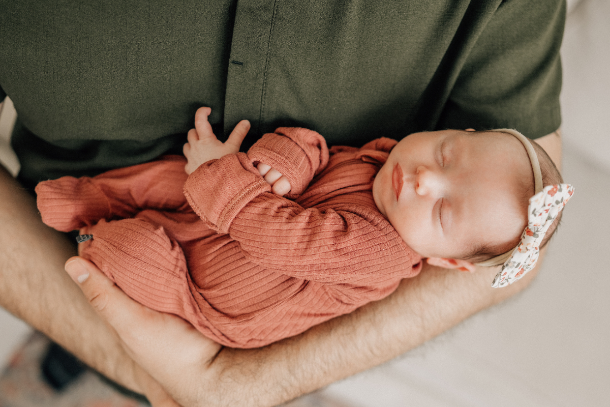 Newborn baby sleeping peacefully while cradled in a parent’s arms, captured during an in-home newborn photography session at home.
