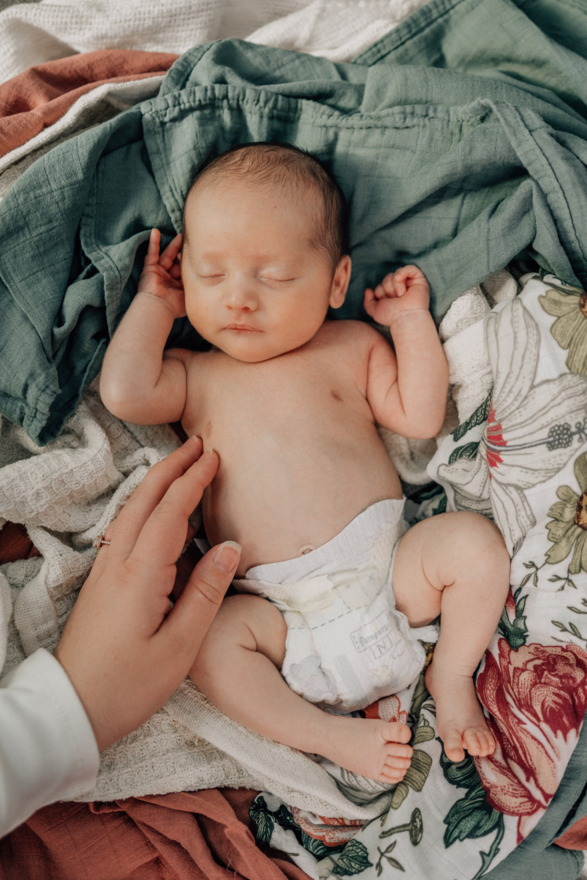 Newborn lying on a soft blanket with a parent’s hand nearby, captured during an in-home newborn photography session at home.