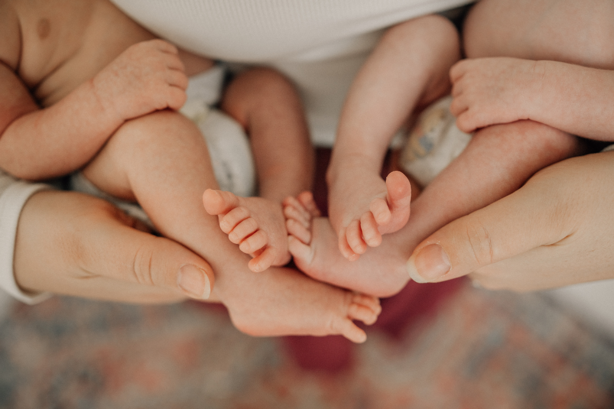 Close-up of twin newborn feet resting in a parent’s hands during an in-home newborn photography session.