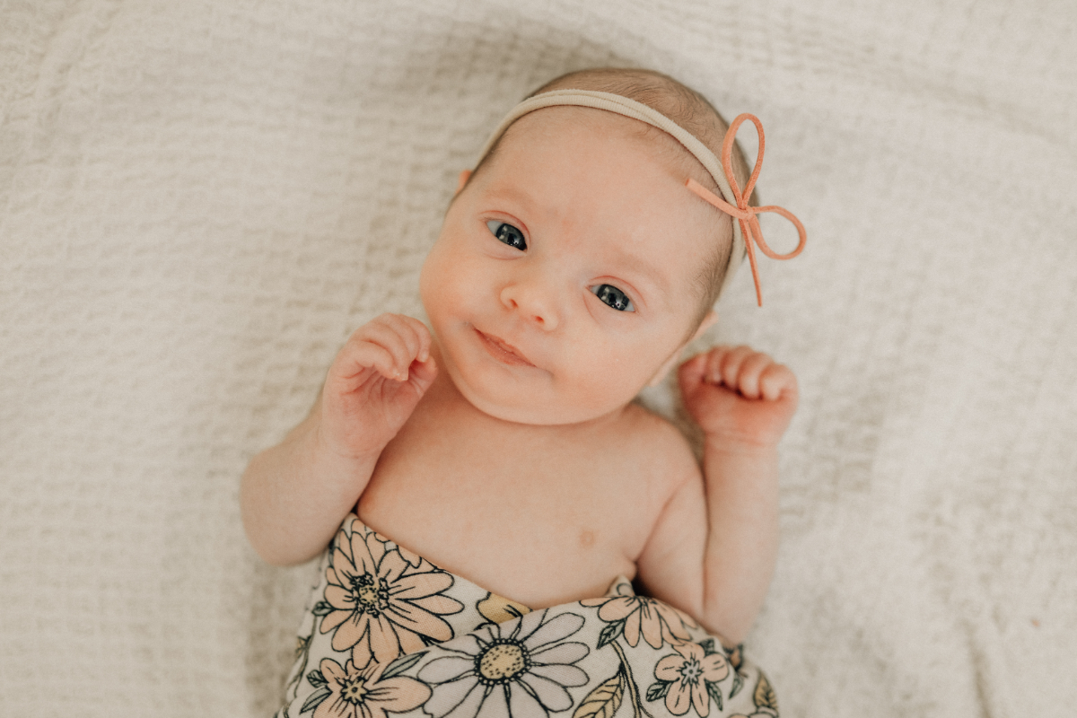Awake newborn lying on a textured blanket, looking toward the camera with a soft expression.