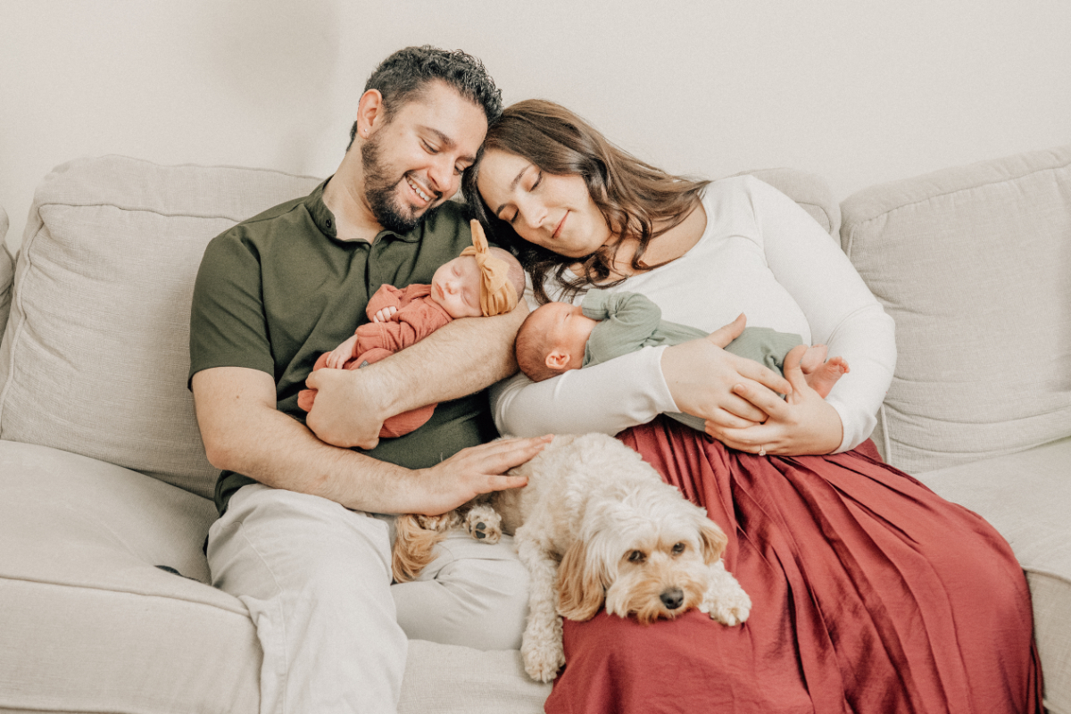 Parents snuggling their newborn on the couch with their dog at their feet during a relaxed in-home newborn photography session.