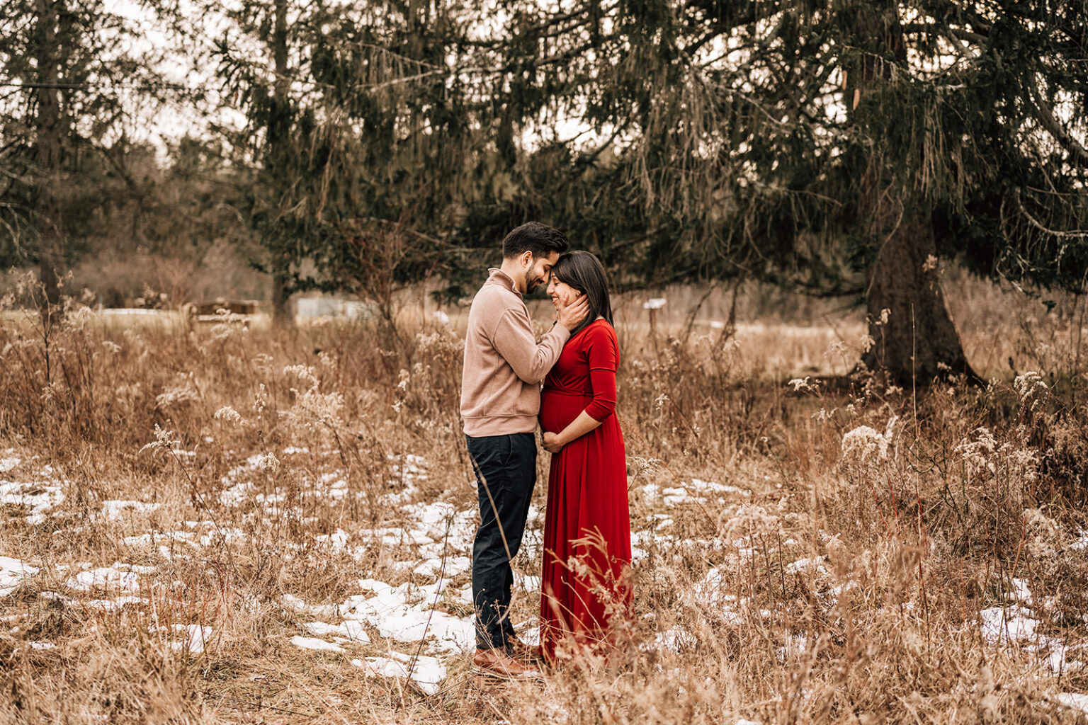 Couple sharing a quiet moment in a winter field, documenting the first year of newborn photos.