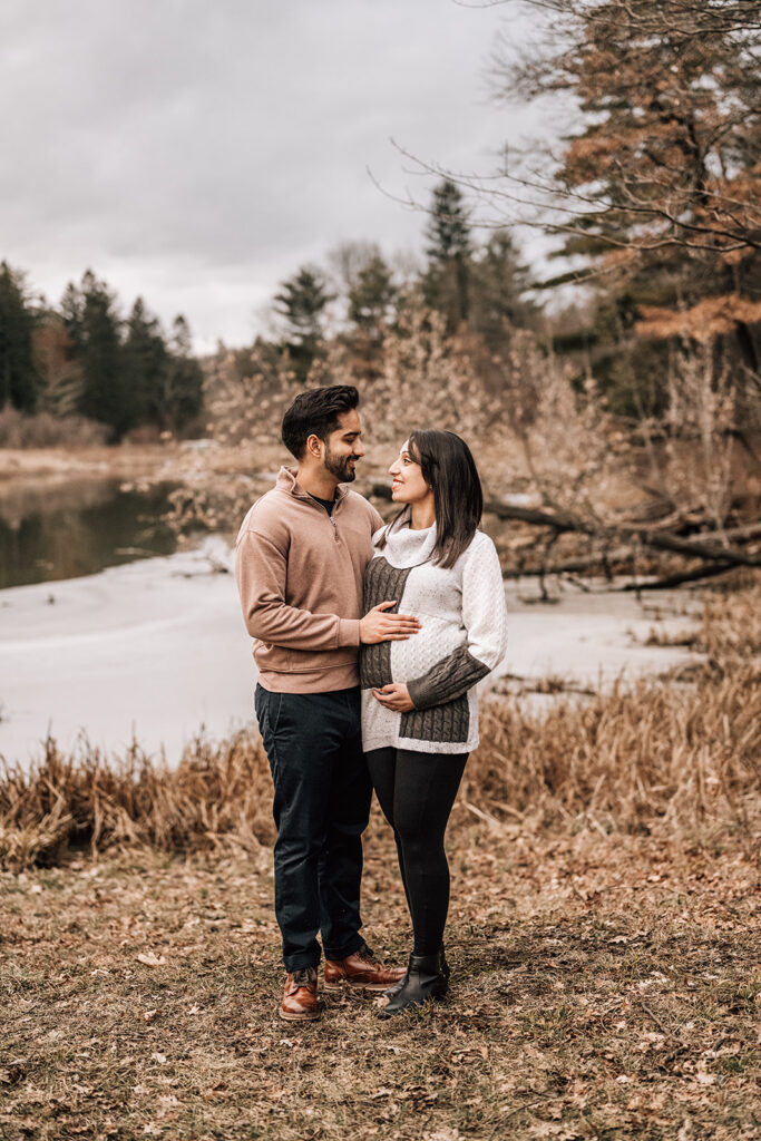 Expecting parents standing by water during maternity session, part of the first year of newborn photos.
