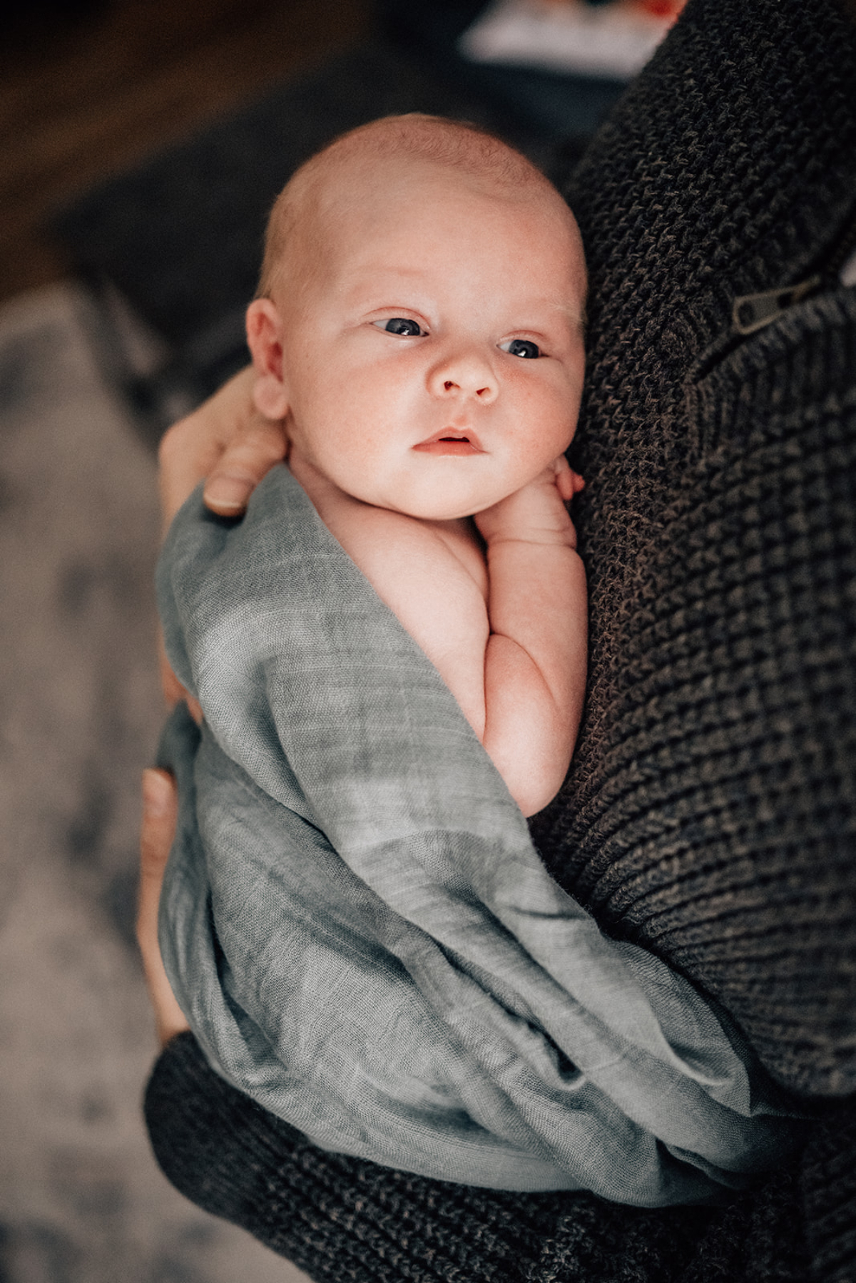 Awake newborn resting on parent’s shoulder during milestone photography session, documenting quiet alert moments at home.