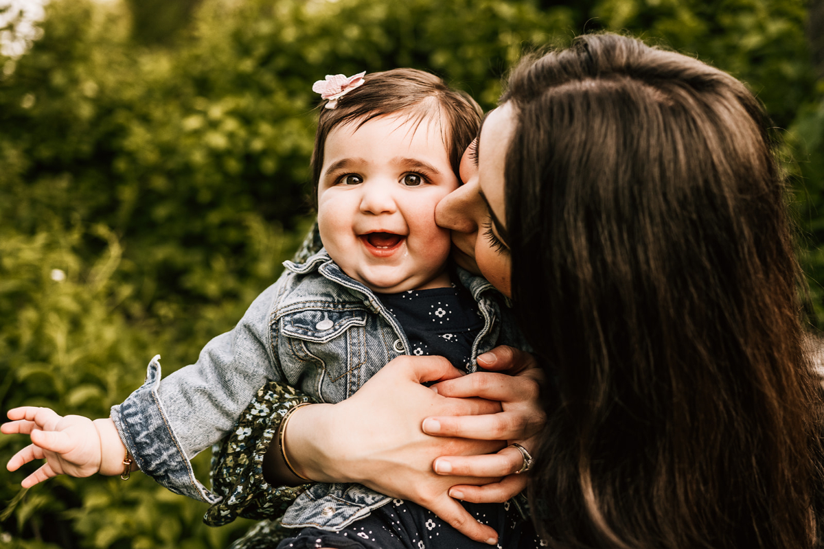 Parent kissing baby’s cheek outdoors, capturing joy, connection, and a playful expression in natural light.