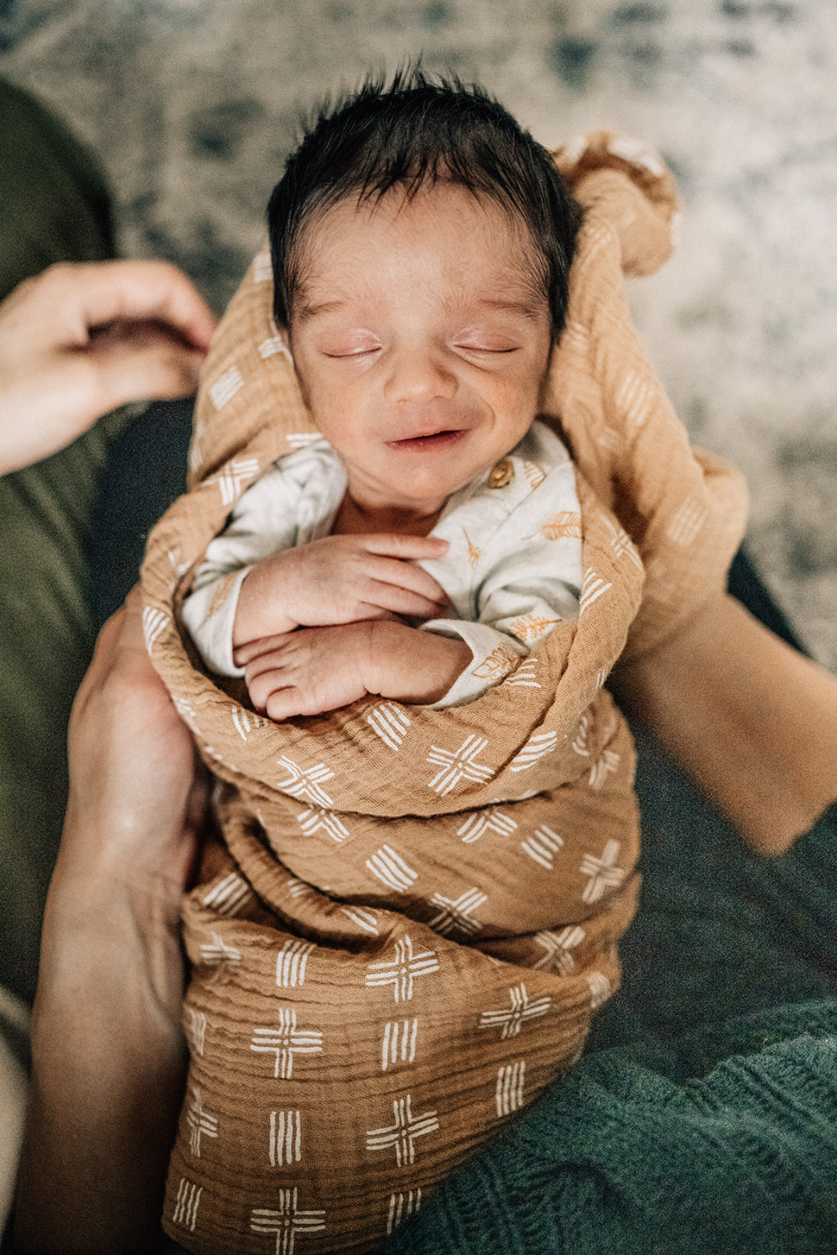 Swaddled newborn smiling softly in parent’s arms during milestone photography session, capturing tenderness and early personality.