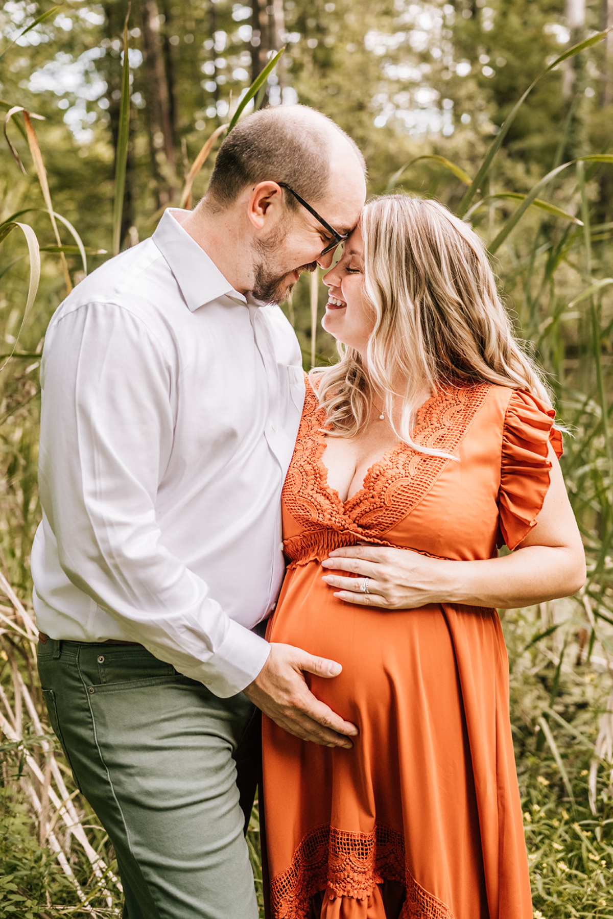 Expecting couple sharing a close moment in tall grass during milestone photography maternity session outdoors.