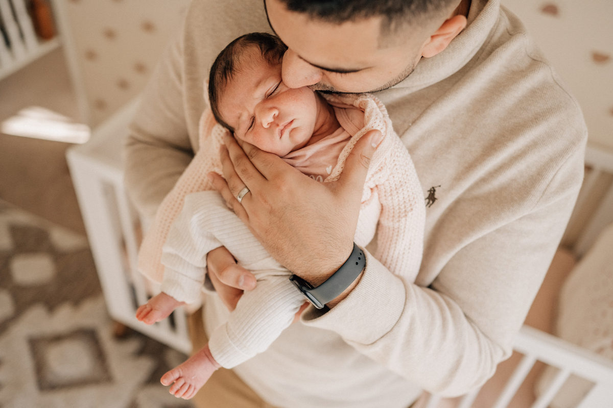 Sleeping newborn cradled in parent’s arms during milestone photography session, capturing tenderness, connection, and early days at home.