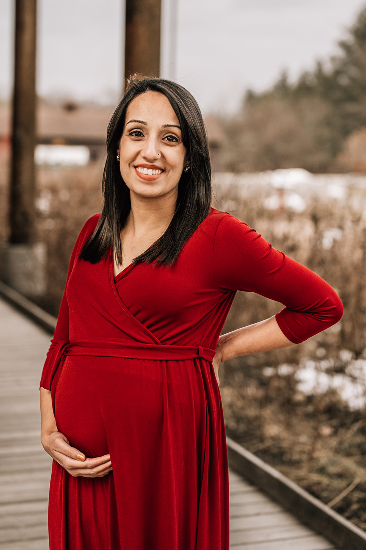 Pregnant woman in red dress smiling outdoors during milestone photography session, celebrating pregnancy and connection.