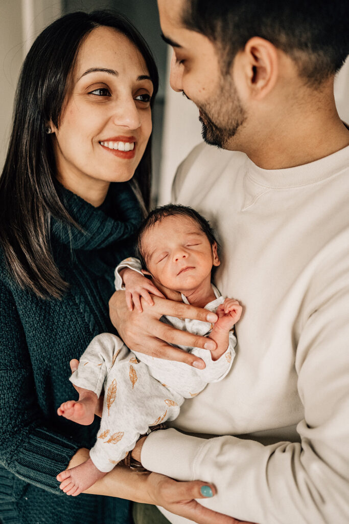 Parents holding newborn together at home, documenting connection during the first year of newborn photos.