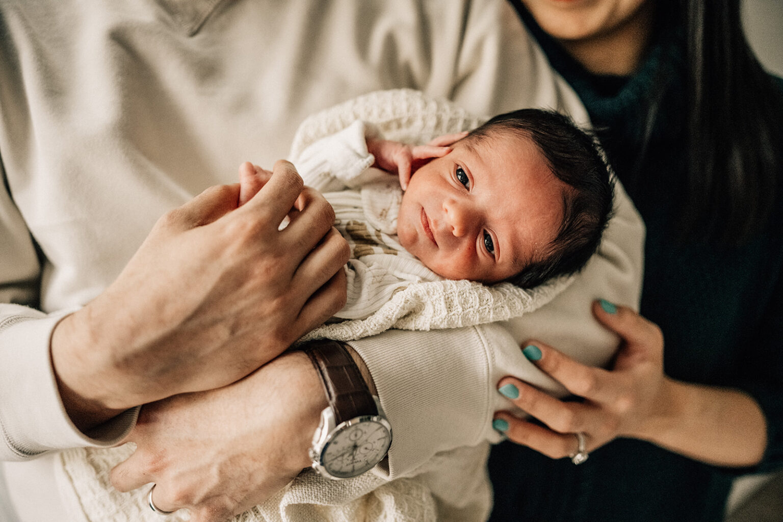 Parent gently holding newborn on bed, showing connection during the first year of newborn photos.
