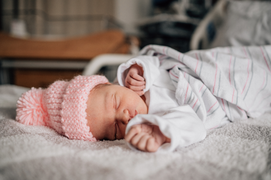 Sleeping newborn wearing a pink knit hat, photographed in the hospital during fresh 48 photos that capture the quiet first hours after birth.