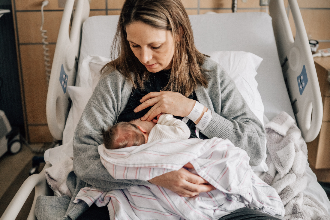 Mother holding her newborn close on a hospital bed, wrapped in a striped blanket during the first quiet hours after birth.