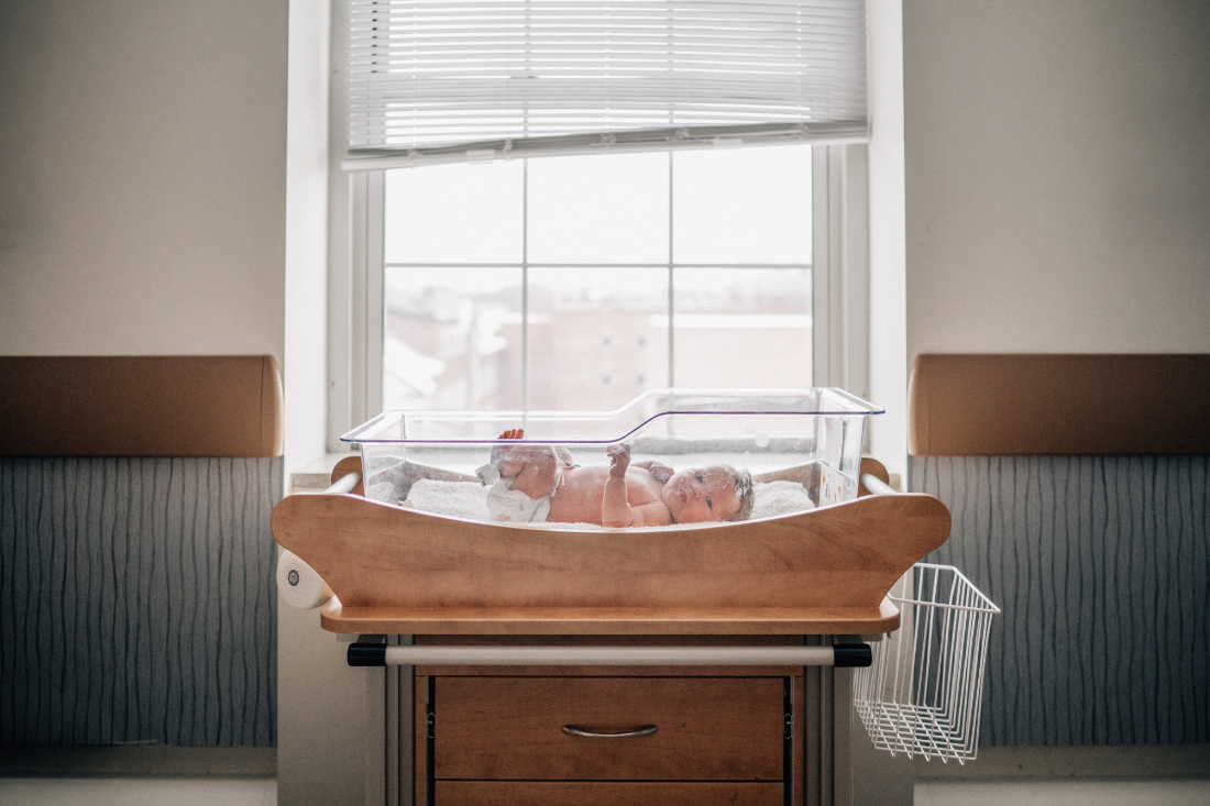 Newborn resting in a hospital bassinet near a window, photographed as part of fresh 48 photos in natural light.