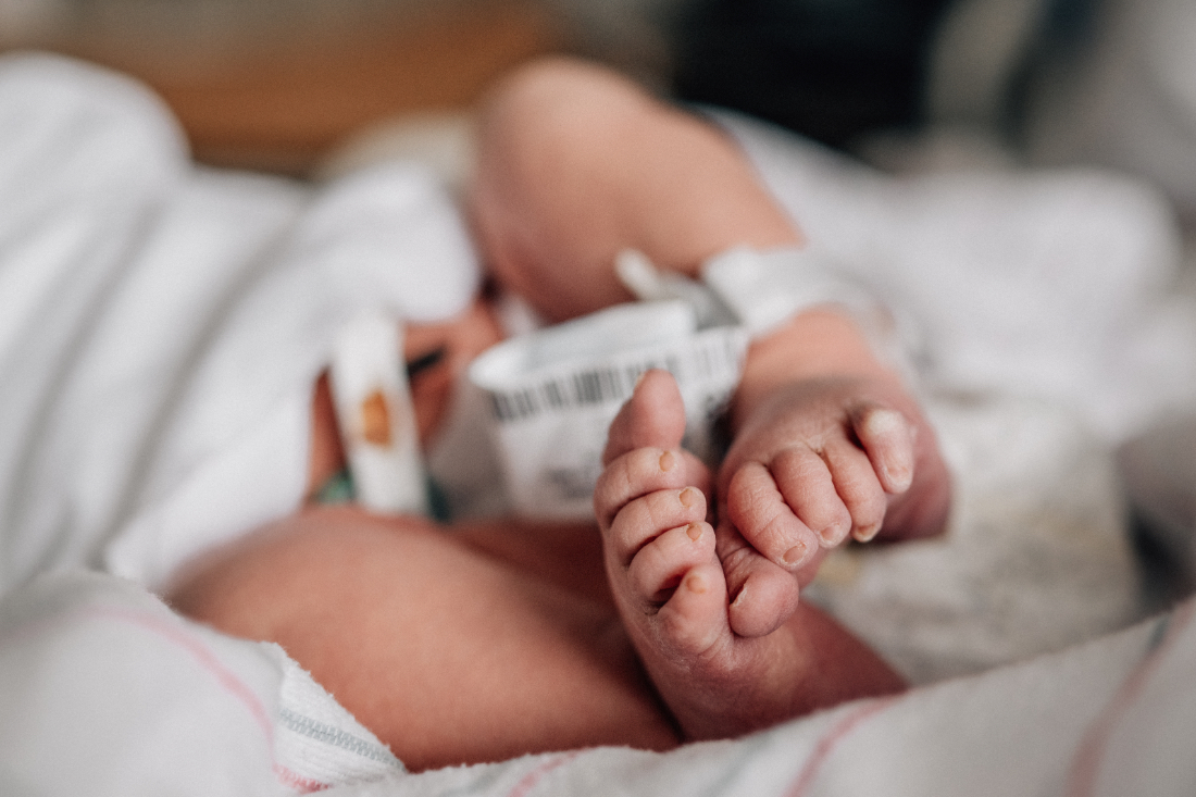 Close-up of newborn feet with hospital ID bracelet resting on a striped blanket in a hospital bassinet.