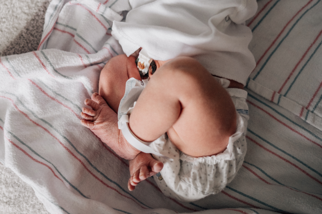 Newborn curled up on a hospital blanket, showing tiny legs and belly during a fresh 48 photo session.