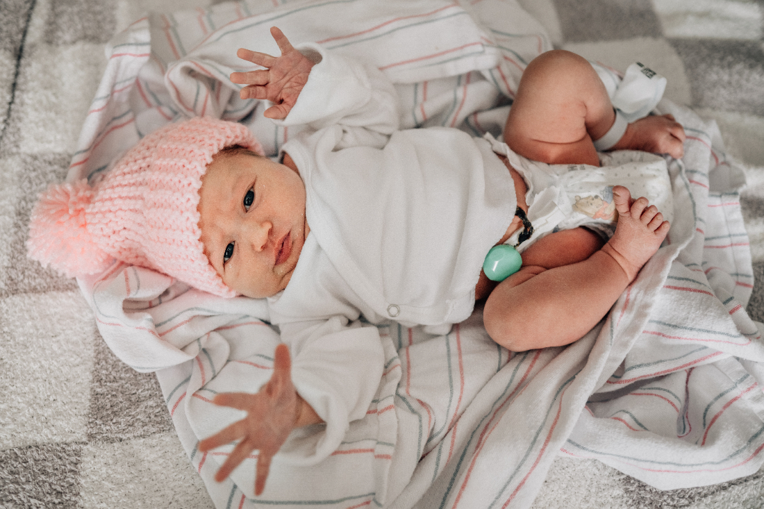 Awake newborn stretching arms while lying on a hospital blanket, captured as part of fresh 48 photos documenting the first day of life.