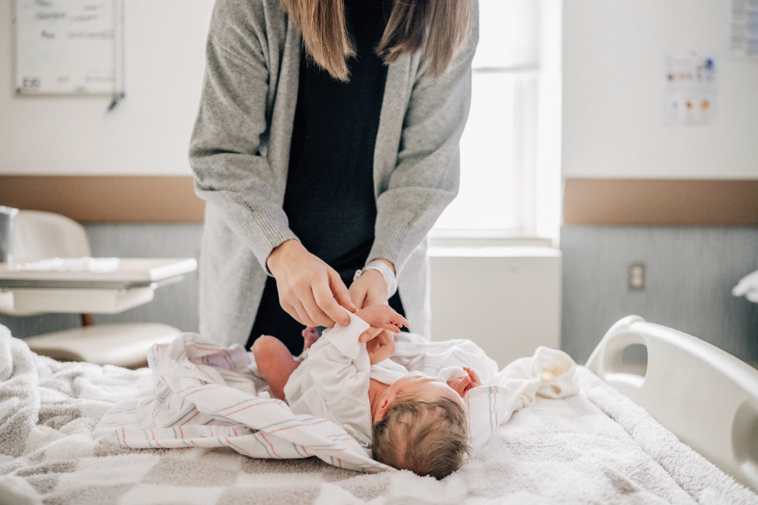 Parent changing newborn’s clothes on a hospital bed, documenting real moments during fresh 48 photos.