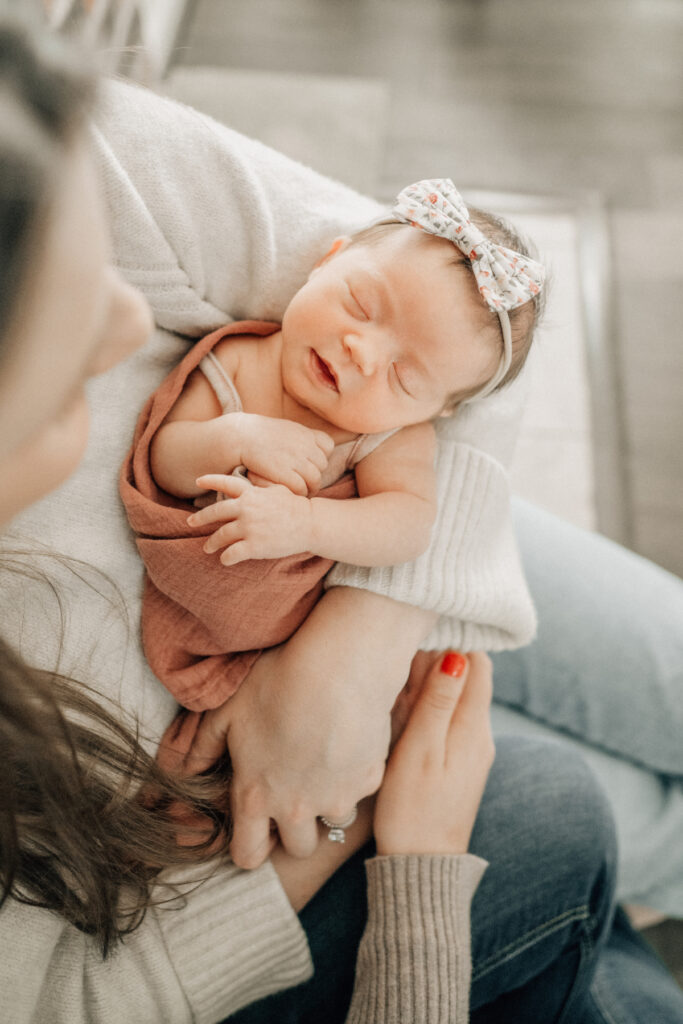 Sleeping baby wrapped in rust swaddle, cradled in parent’s arms.