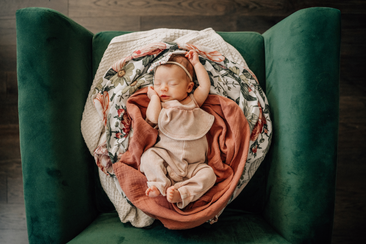 Sleeping baby in beige outfit resting on floral blanket in green chair