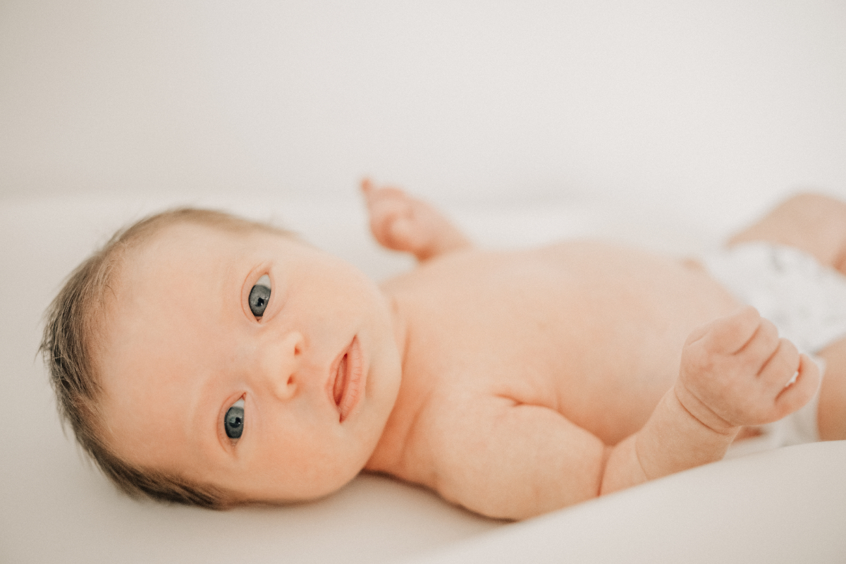 Simple newborn baby photos of baby lying awake on soft white bed.