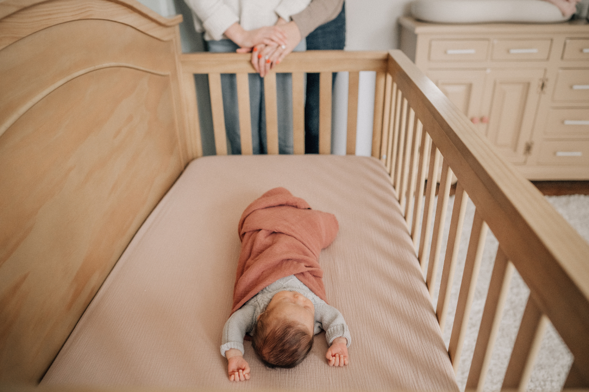 In-home newborn baby photos of swaddled baby sleeping in wooden crib.