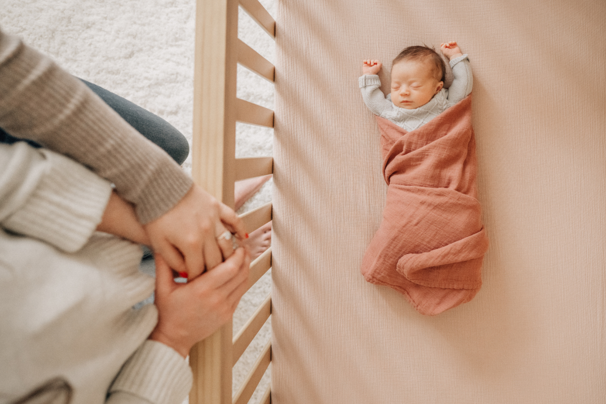 Overhead newborn baby photos of baby wrapped in blanket inside crib.