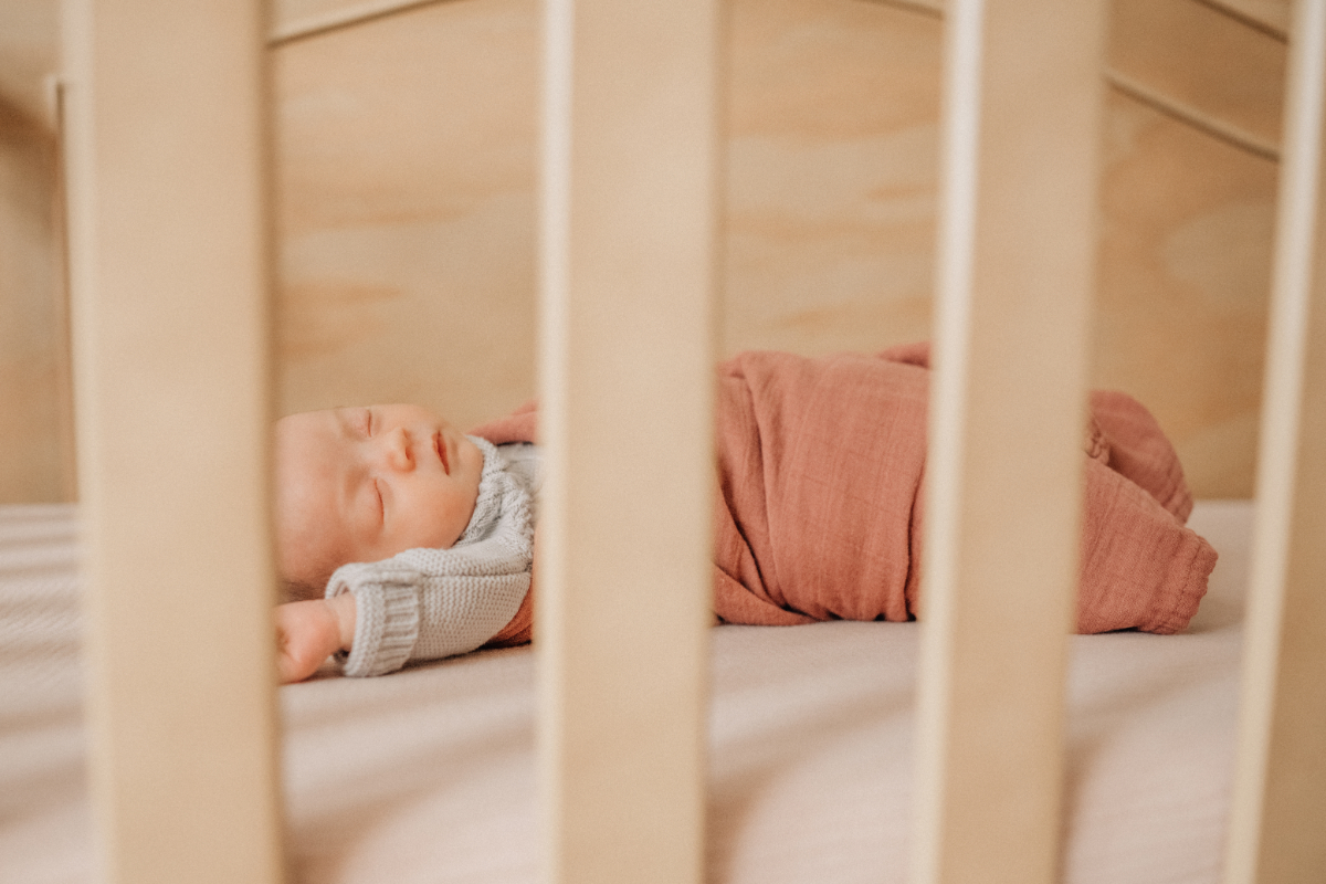 Cozy newborn baby photos of sleeping baby seen through crib slats.