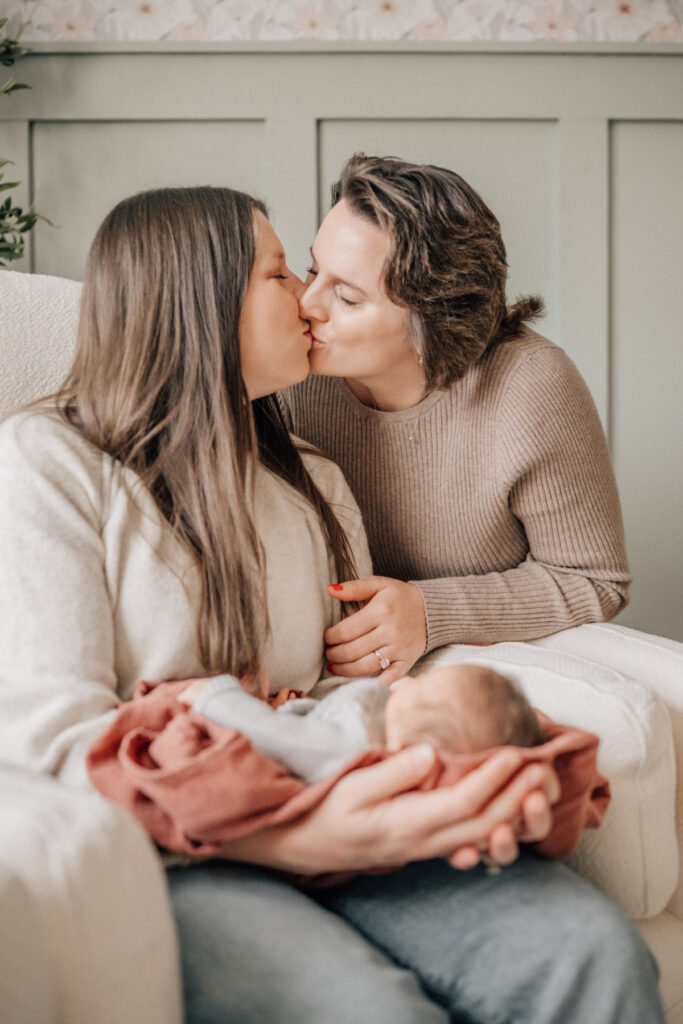 Lifestyle newborn baby photos of two moms sharing a quiet kiss in nursery