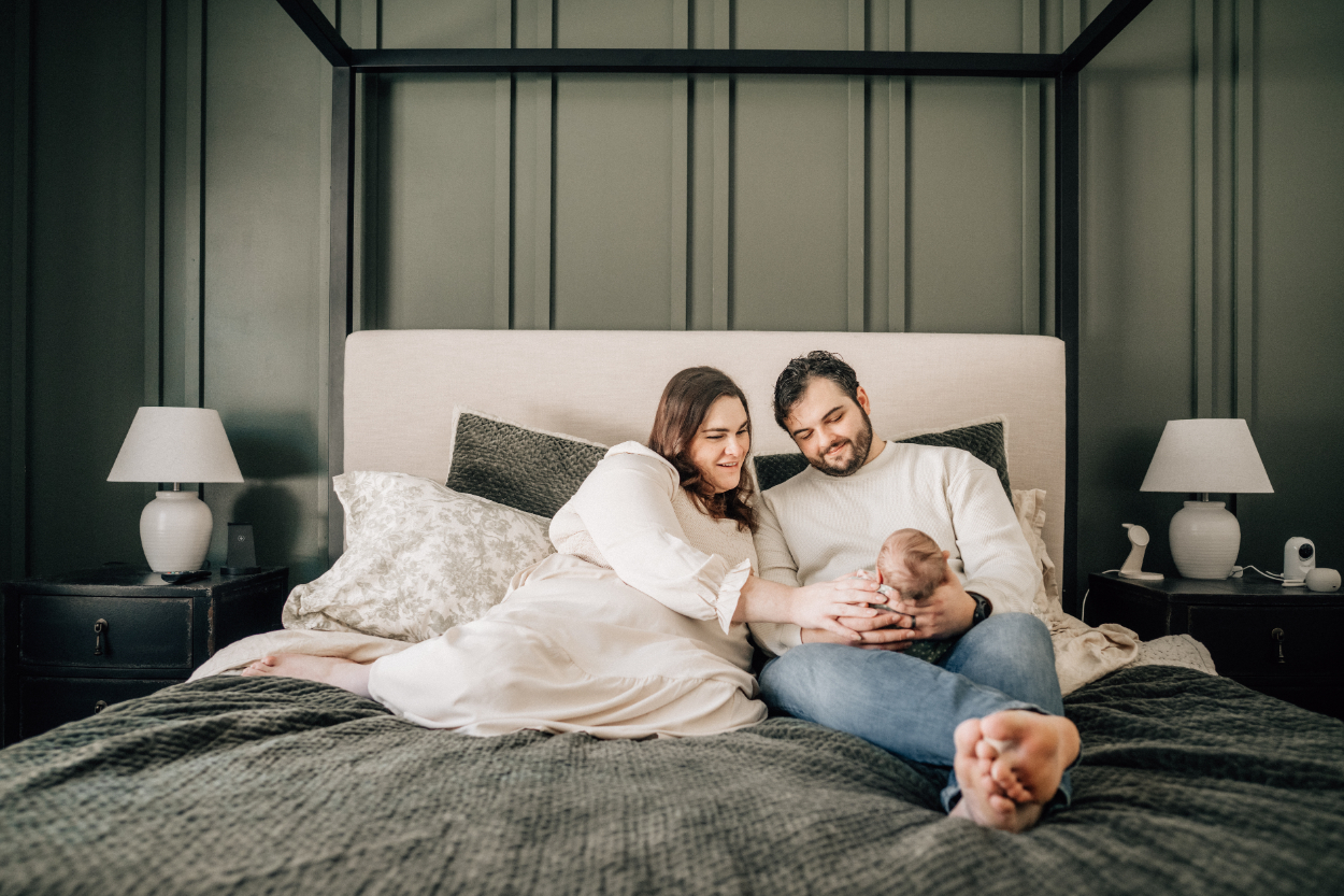 In-home newborn photography ideas with parents cuddling baby on bed in cozy bedroom.