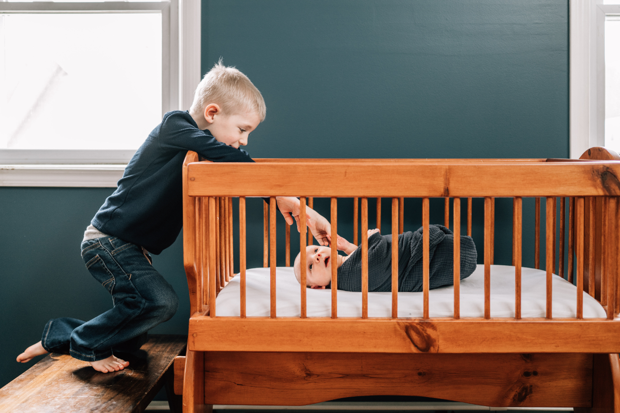 Lifestyle newborn photography ideas showing sibling peeking into crib at baby.