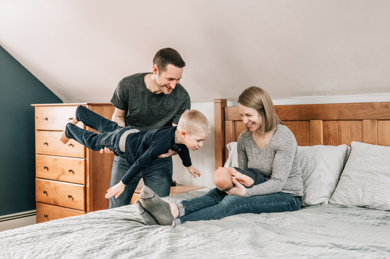 In-home newborn photography ideas with parents and sibling playing on bed.