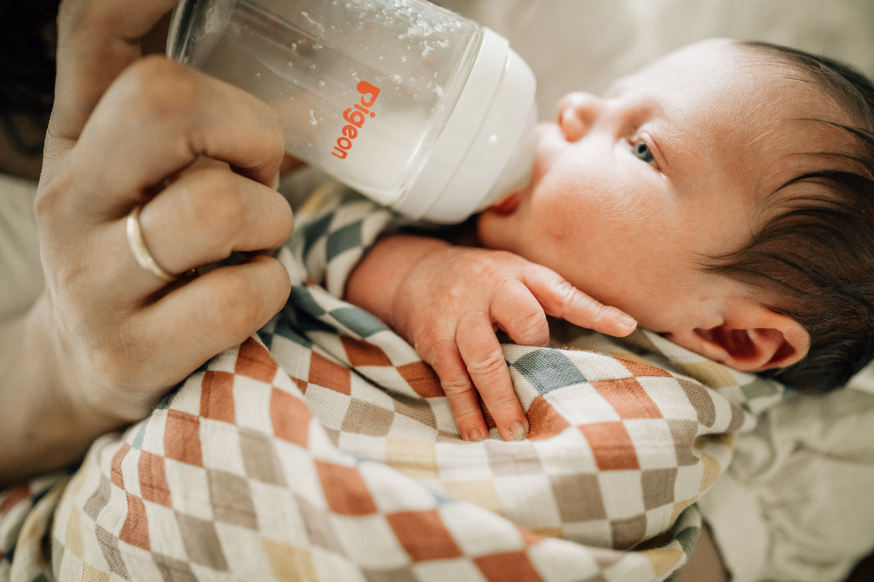 Close-up of newborn being bottle-fed while resting in parent’s arms.