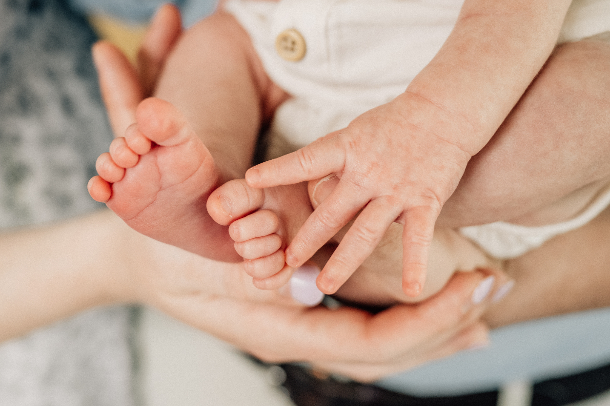 Close-up of baby’s tiny toes and fingers resting gently in parent’s hands.