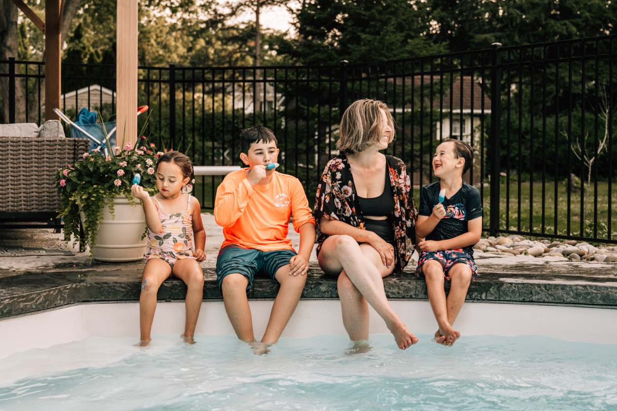 Family sitting by pool eating popsicles, capturing relaxed, candid summer connection and everyday moments