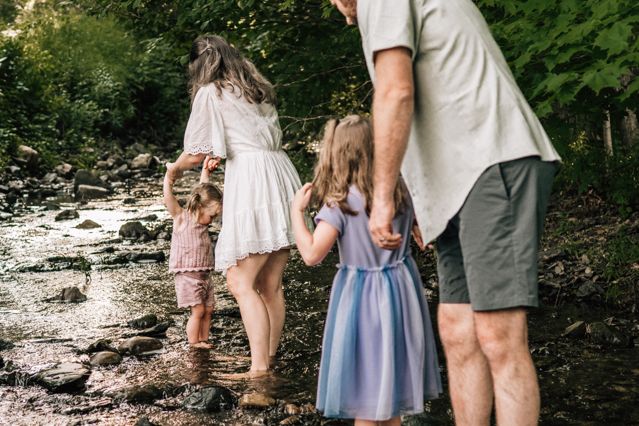 Family walking through shallow creek together, capturing connection, movement, and quiet outdoor exploration