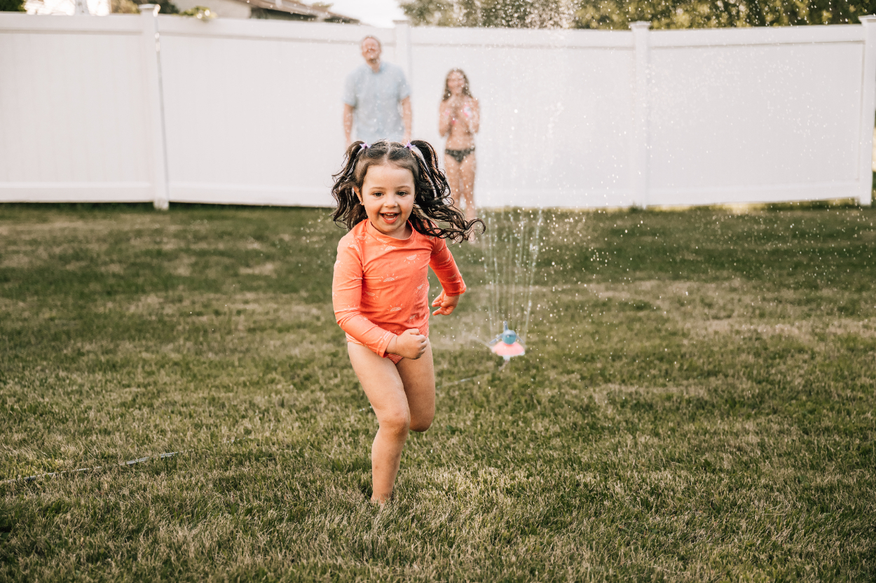 Child running through sprinkler during a backyard photoshoot, showing joyful movement and carefree summer play