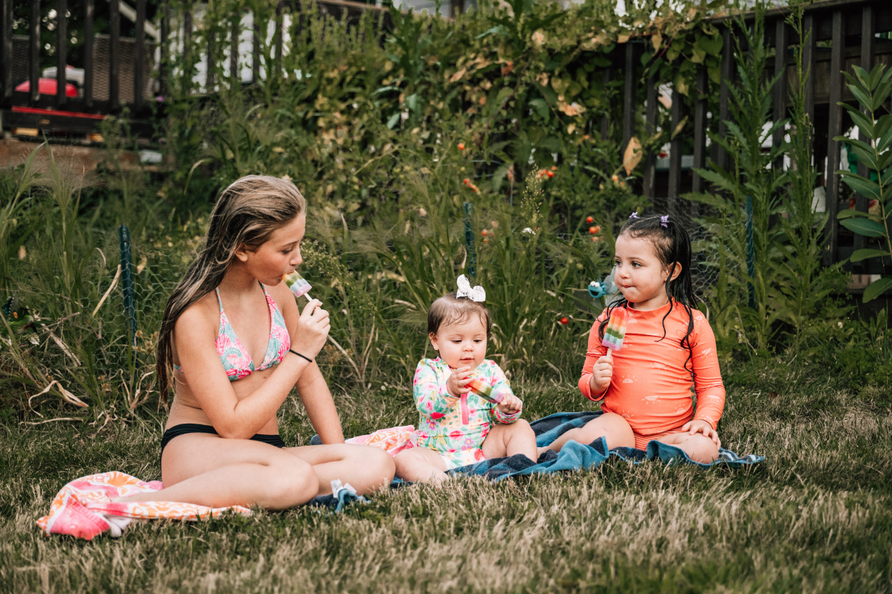 Kids sitting in the grass eating popsicles together, capturing relaxed summer moments and sibling connection