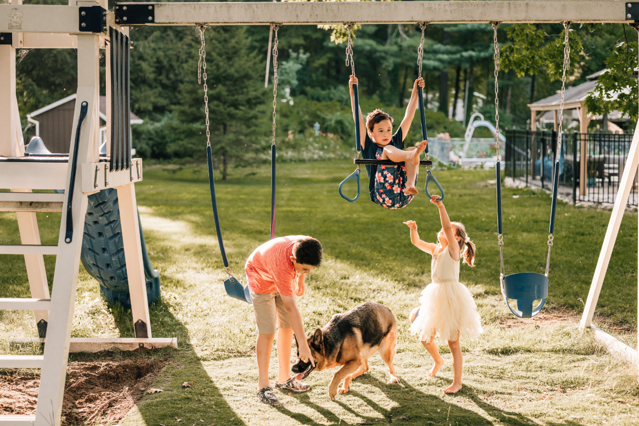 Kids playing under swingset during a backyard photoshoot, filled with movement, sunlight, and playful moments