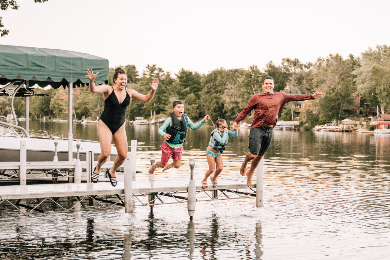 Family jumping off dock into lake together, capturing joyful, energetic summer moments and shared adventure