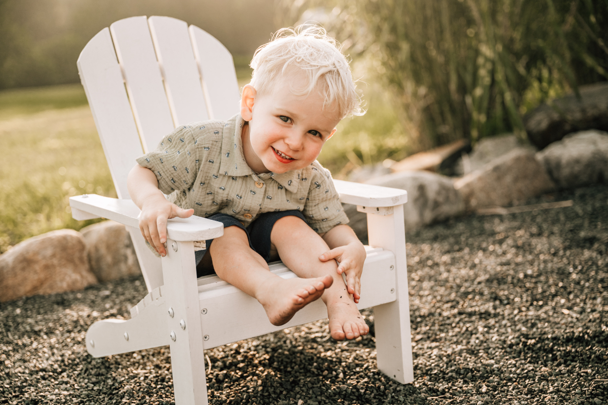 Toddler sitting in outdoor chair smiling, capturing soft, quiet moment in warm evening light