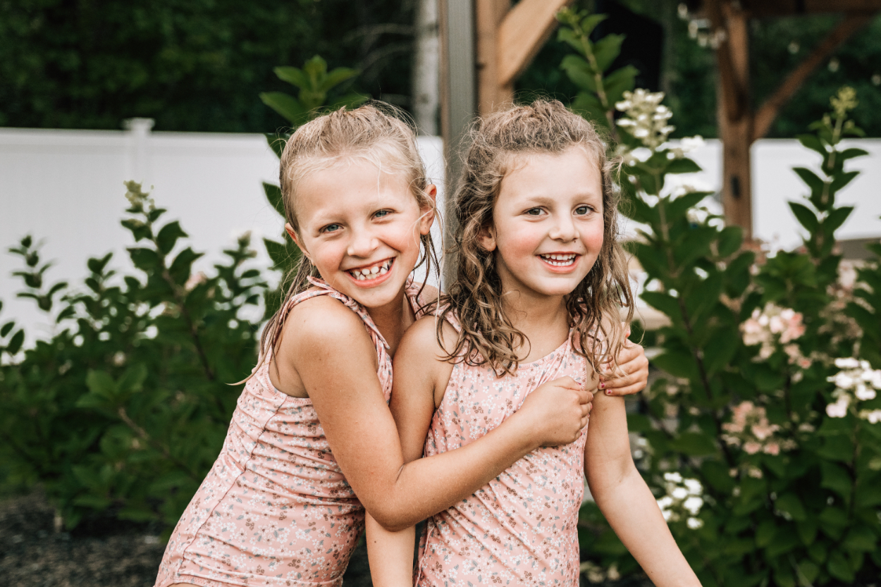 Two girls hugging and smiling in the yard, capturing joyful sibling connection and playful summer moments