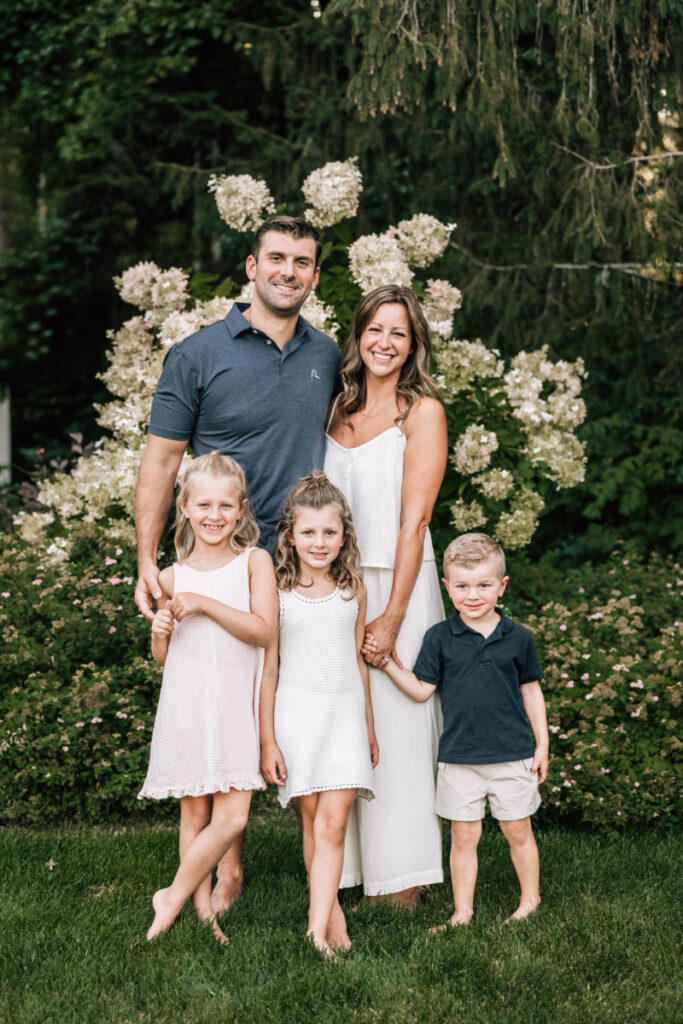 Family standing together with three children in garden during relaxed outdoor family portraits session in Albany NY.