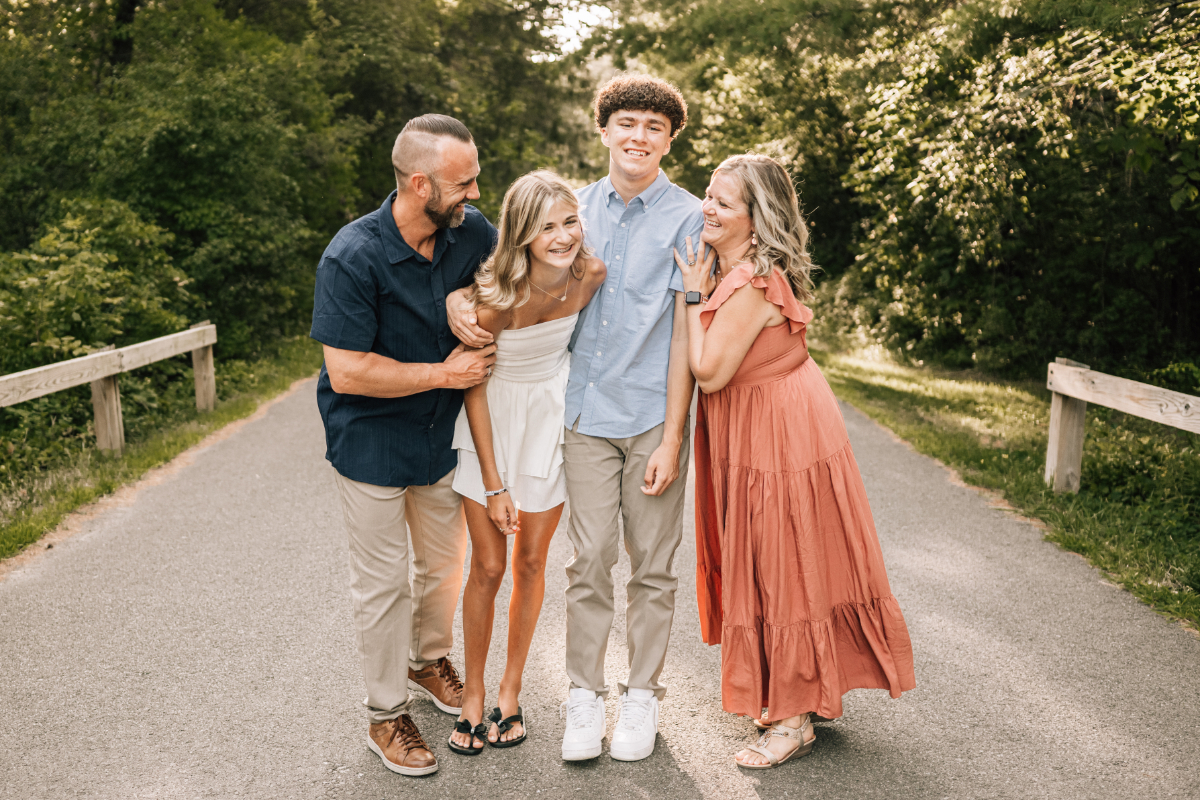 Family of four walking together on path, laughing and leaning in close during relaxed outdoor moment