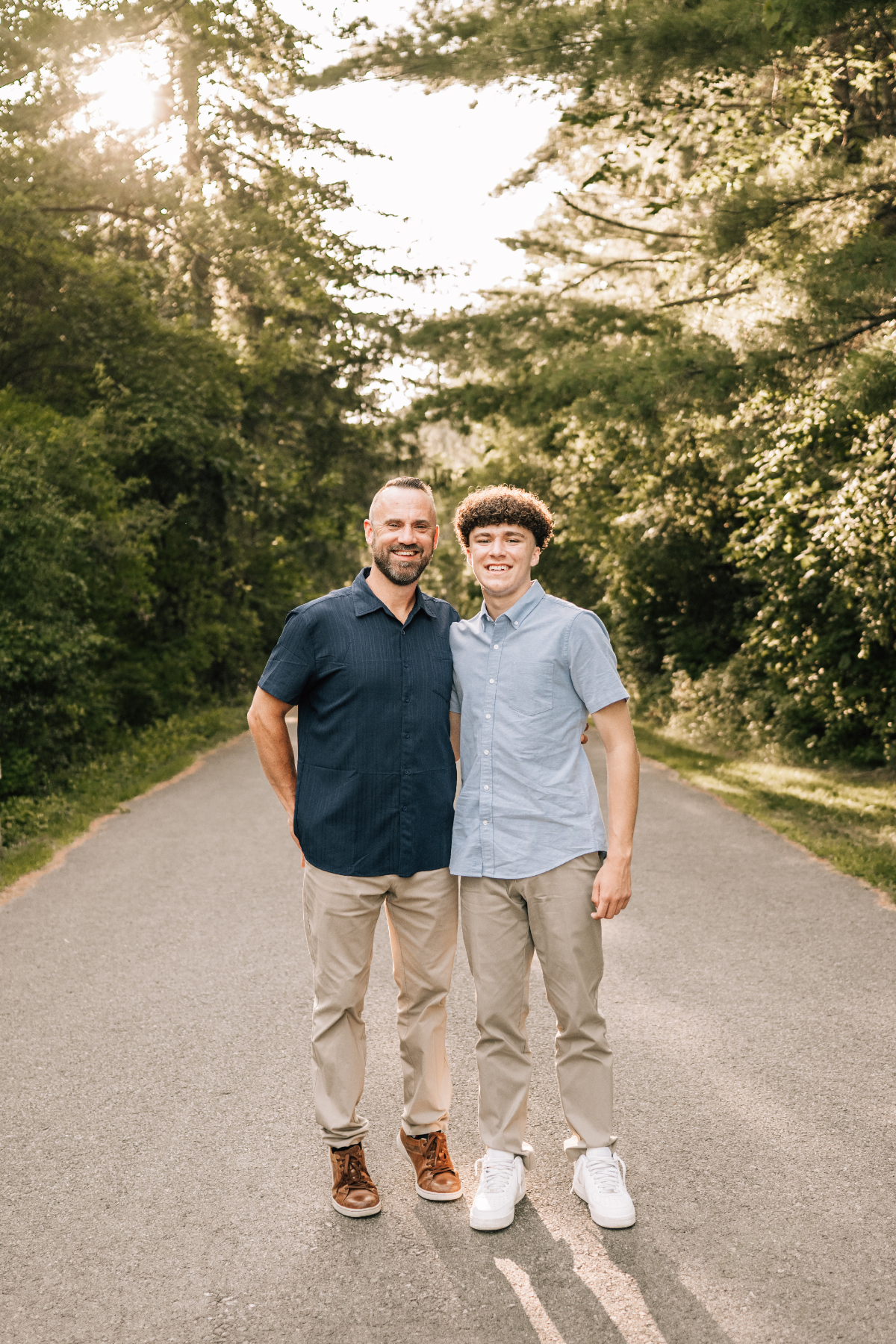 Senior pictures of teen with dad walking on tree-lined path, relaxed outdoor family moment