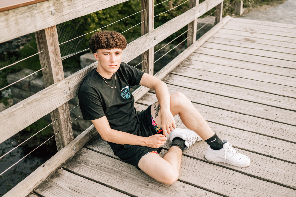 Teen boy sitting on wooden bridge, relaxed pose with casual outfit and natural outdoor setting